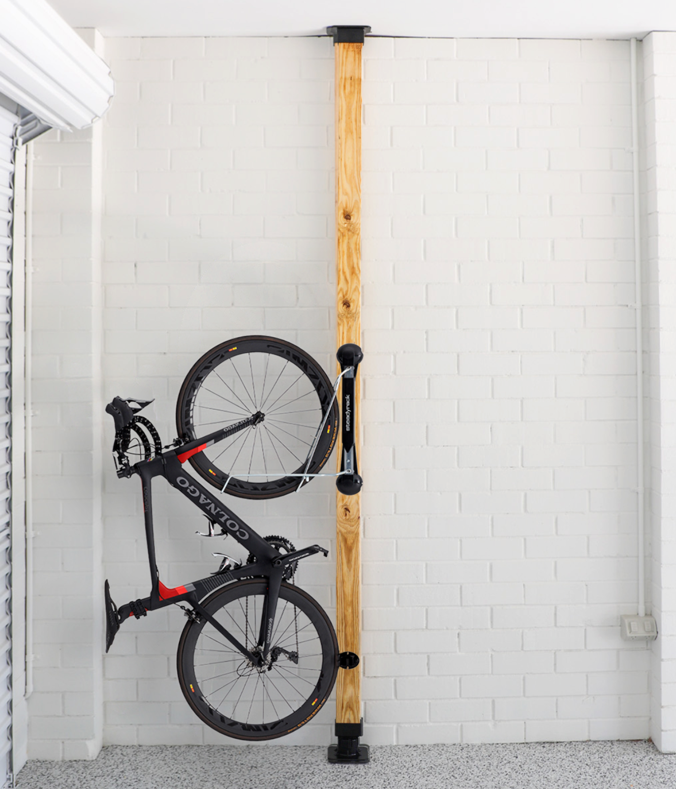 Bicycle hanging on a wooden stand against a white brick wall.